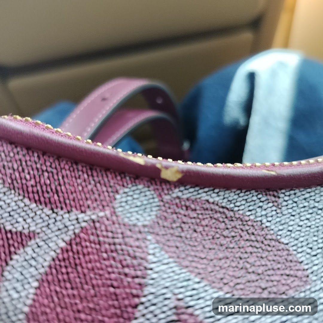 A close-up shot of the top edge of a bag with a patterned fabric. The bag has burgundy leather handles and a burgundy trim around the top. There are some small yellowed scuff marks on the trim. In the background, out of focus, is a blue item, possibly clothing.