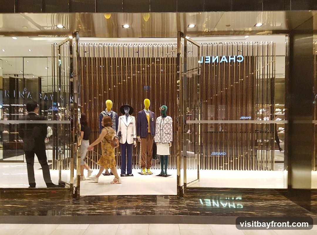 The exterior of a Chanel store with mannequins displaying outfits in the window. The Chanel logo is visible on the glass facade.