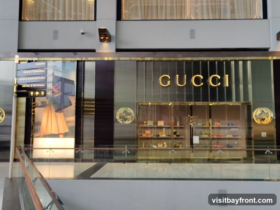 The exterior of a Gucci store with the brand name prominently displayed in gold lettering above a display window. The window showcases various merchandise. To the left, a directional sign indicates 'CASINO', 'COACH TERMINAL', 'EXPO & CONVENTION', and 'HOTEL & SKYPARK'.