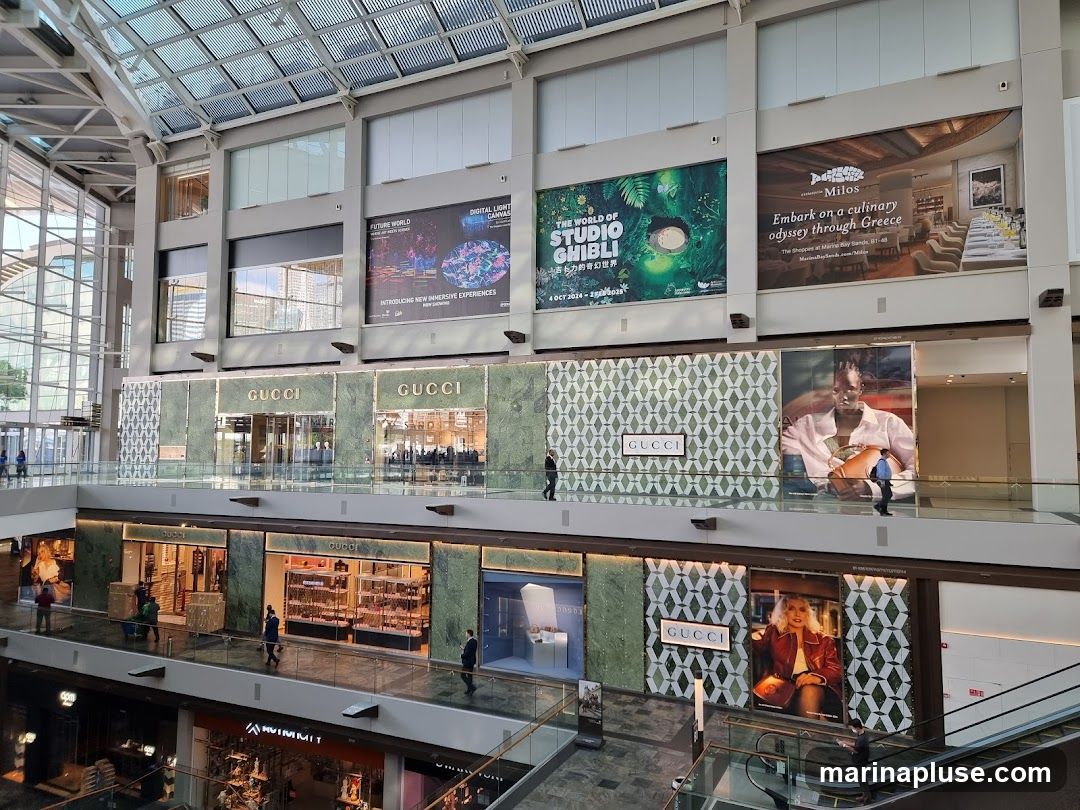 The image shows the interior of a multi-level shopping mall. On the upper level, there are large advertisements for