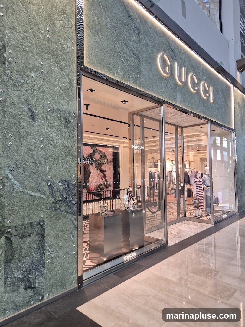 The exterior of a Gucci store with a green marble facade. The Gucci logo is illuminated above the entrance, which features glass doors and windows displaying merchandise and mannequins.