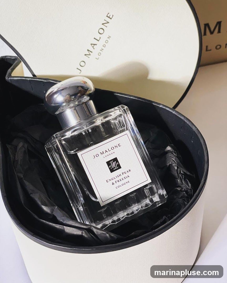 A bottle of Jo Malone English Pear & Freesia Cologne is presented in a gift box lined with black tissue paper. The box and bottle feature the Jo Malone London branding.