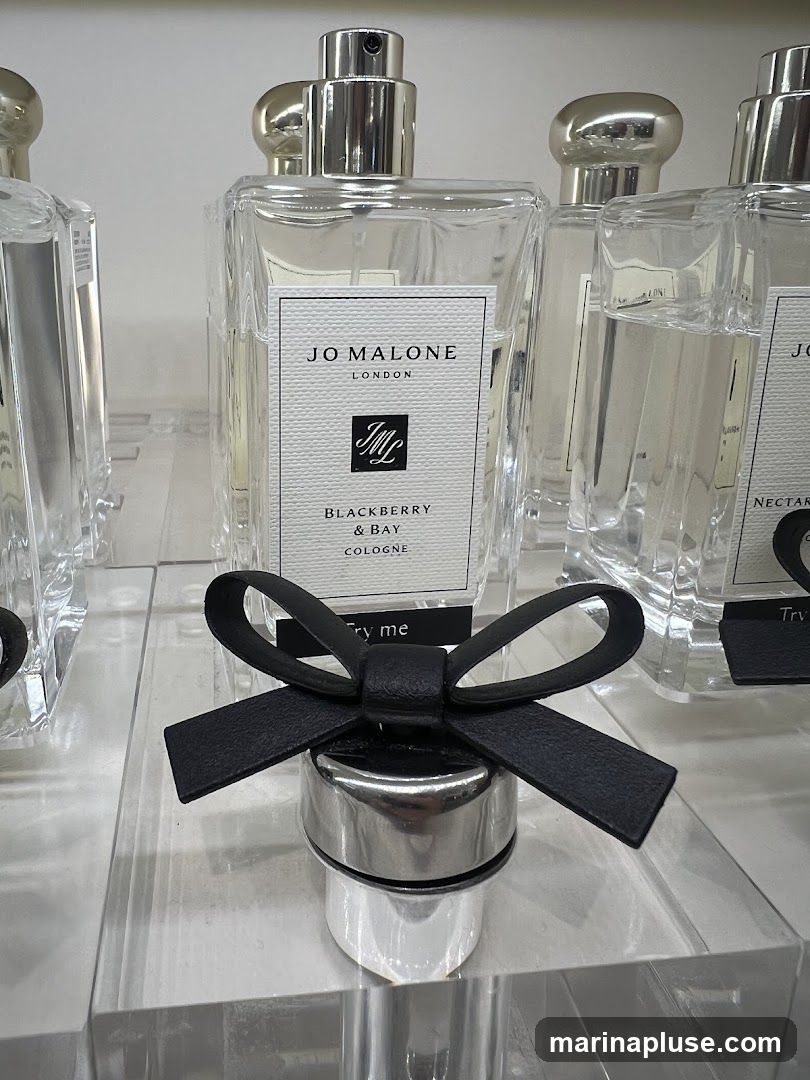 A close-up shot of Jo Malone perfumes on display. The central bottle is labeled "JO MALONE LONDON" and features "BLACKBERRY & BAY COLOGNE" with the brand's crest. A silver cap with a black leather bow is prominently displayed in the foreground, with the text "Try me" visible on a small black tag attached to it. Other Jo Malone bottles are visible in the background.