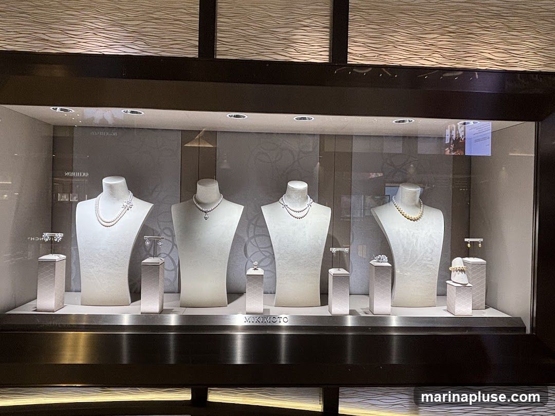 A display window showcases pearl necklaces and earrings on mannequins and stands. The brand name 'MIKIMOTO' is visible on a shelf below the display.