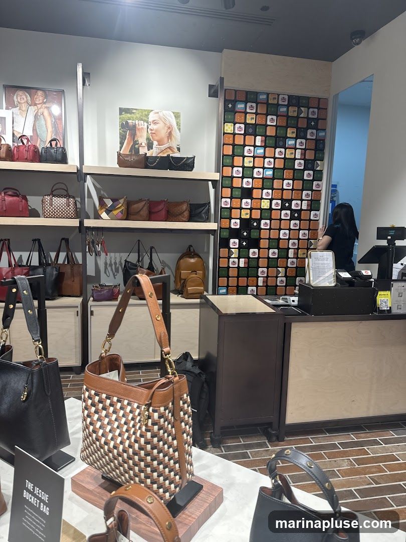 A view inside a store displaying various handbags on shelves and display stands. A cashier is visible at a counter in the background. The walls are decorated with a mosaic of colorful tiles.
