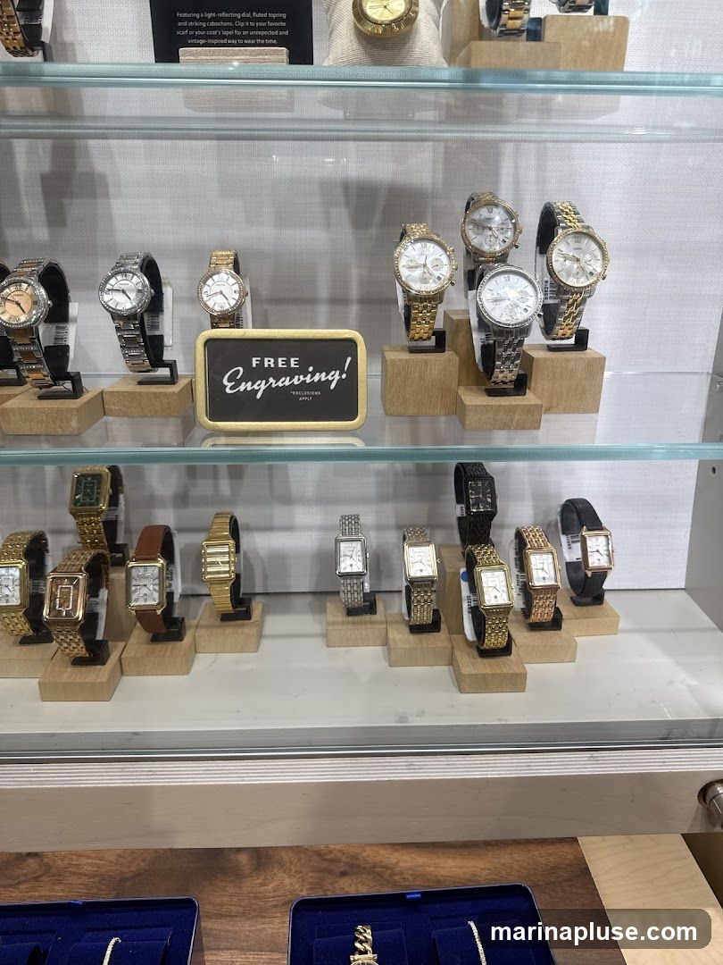A display case filled with various watches. The watches are arranged on wooden stands on two shelves. A sign in the middle of the top shelf reads "FREE Engraving!". Some watches are gold-toned, while others are silver-toned. Some have metal bands, and others have leather bands. The watches vary in style, with some having round faces and others having rectangular faces.