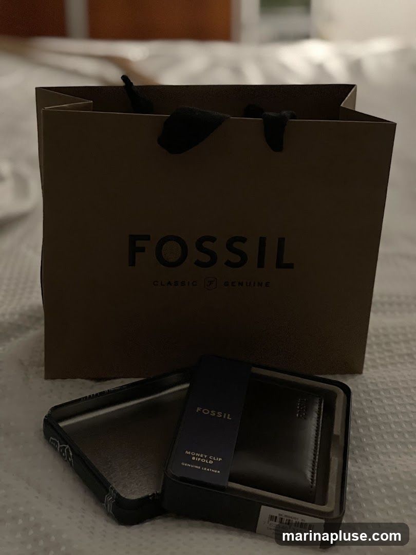 A brown Fossil shopping bag is behind an open tin containing a black Fossil money clip bifold wallet made of genuine leather.