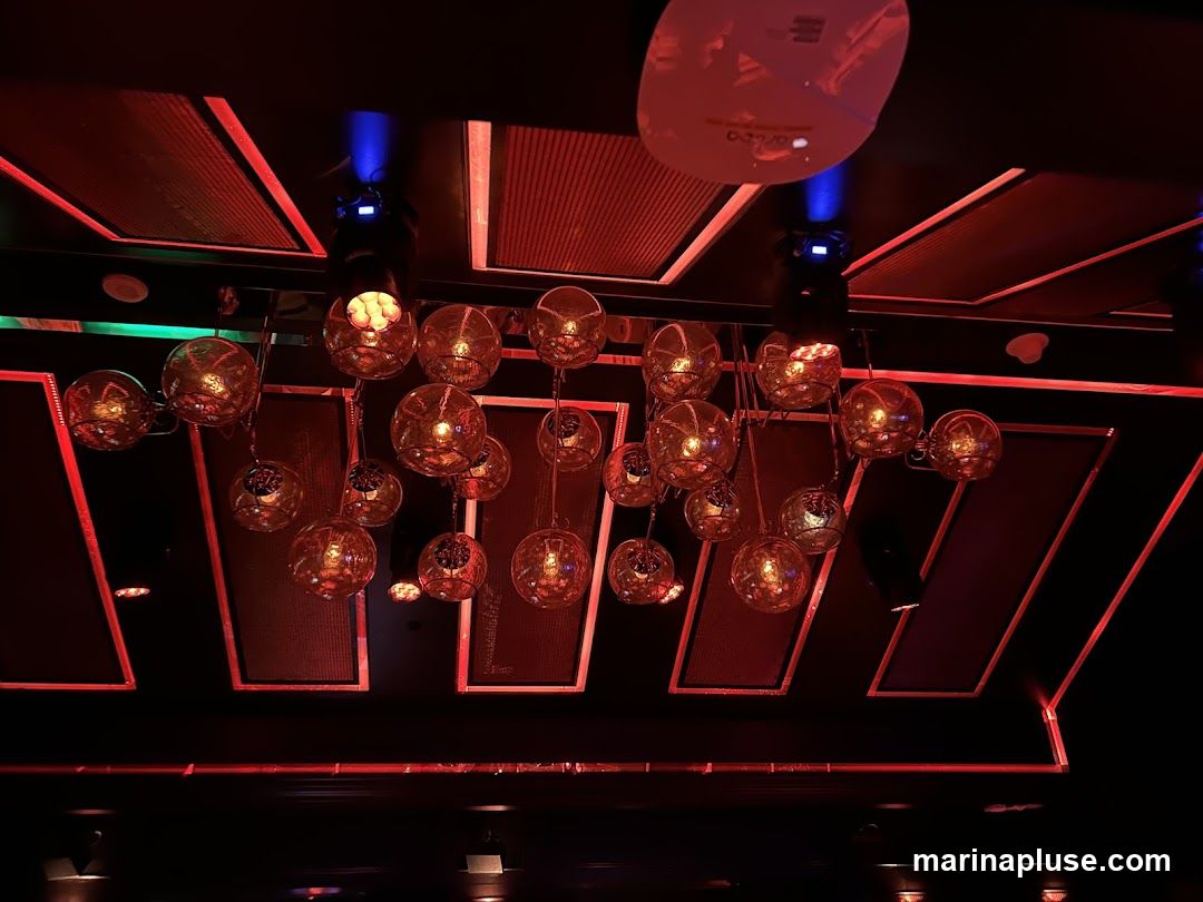 A cluster of spherical glass light fixtures hangs from the ceiling, illuminated by warm, amber light. The ceiling is dark with red and blue accent lighting.