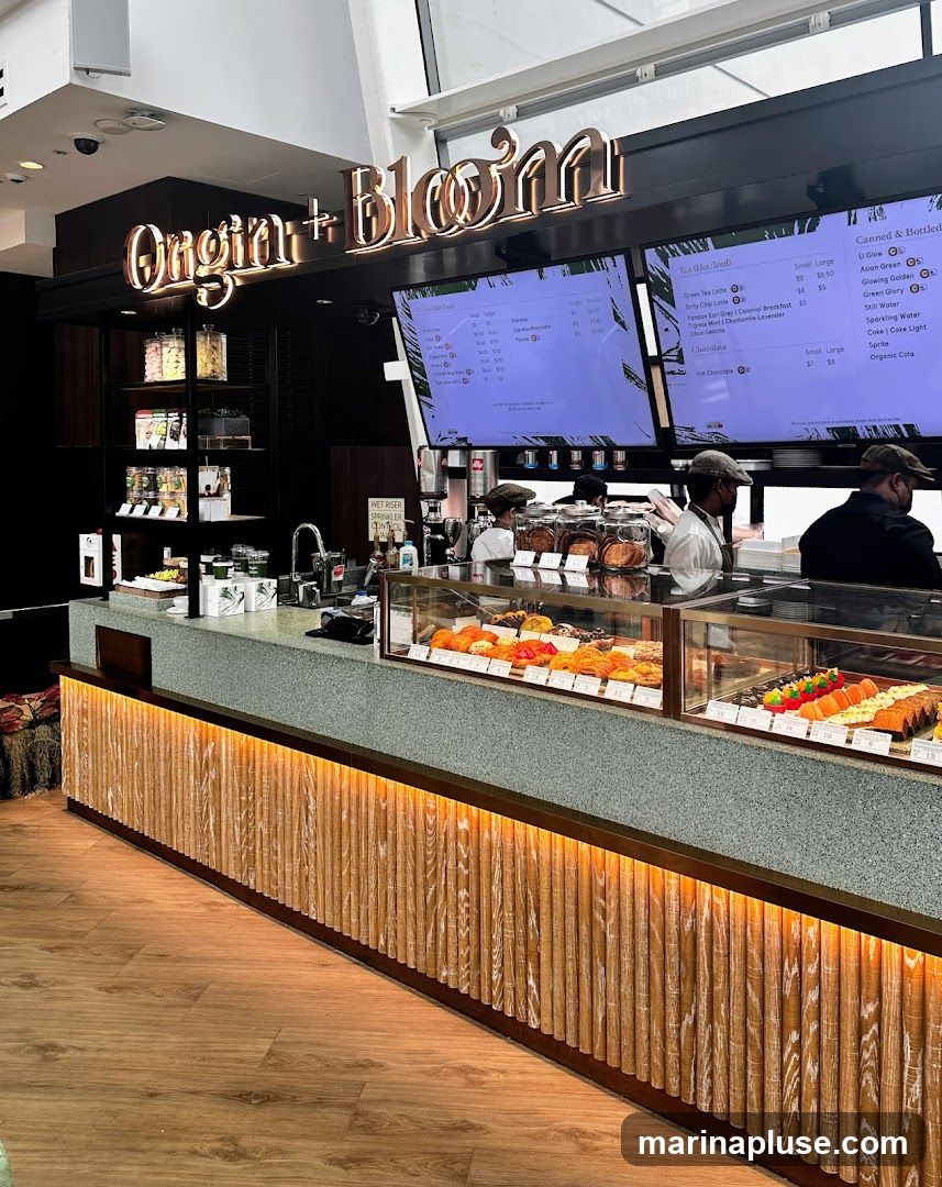 A view of a cafe counter with a display case filled with pastries. Above the counter are large digital screens displaying menu items. The cafe's name,