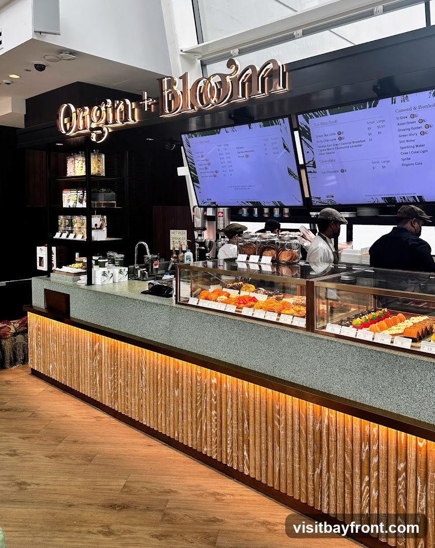 A view of a cafe counter with a display case filled with pastries. Above the counter are large digital screens displaying menu items. The cafe's name,