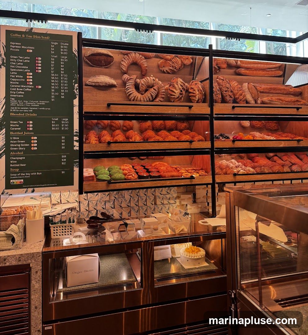 A display case filled with various baked goods, including croissants, breads, and pastries. A menu board is visible on the left side, listing coffee, tea, blended drinks, juices, alcohol, and soup.
