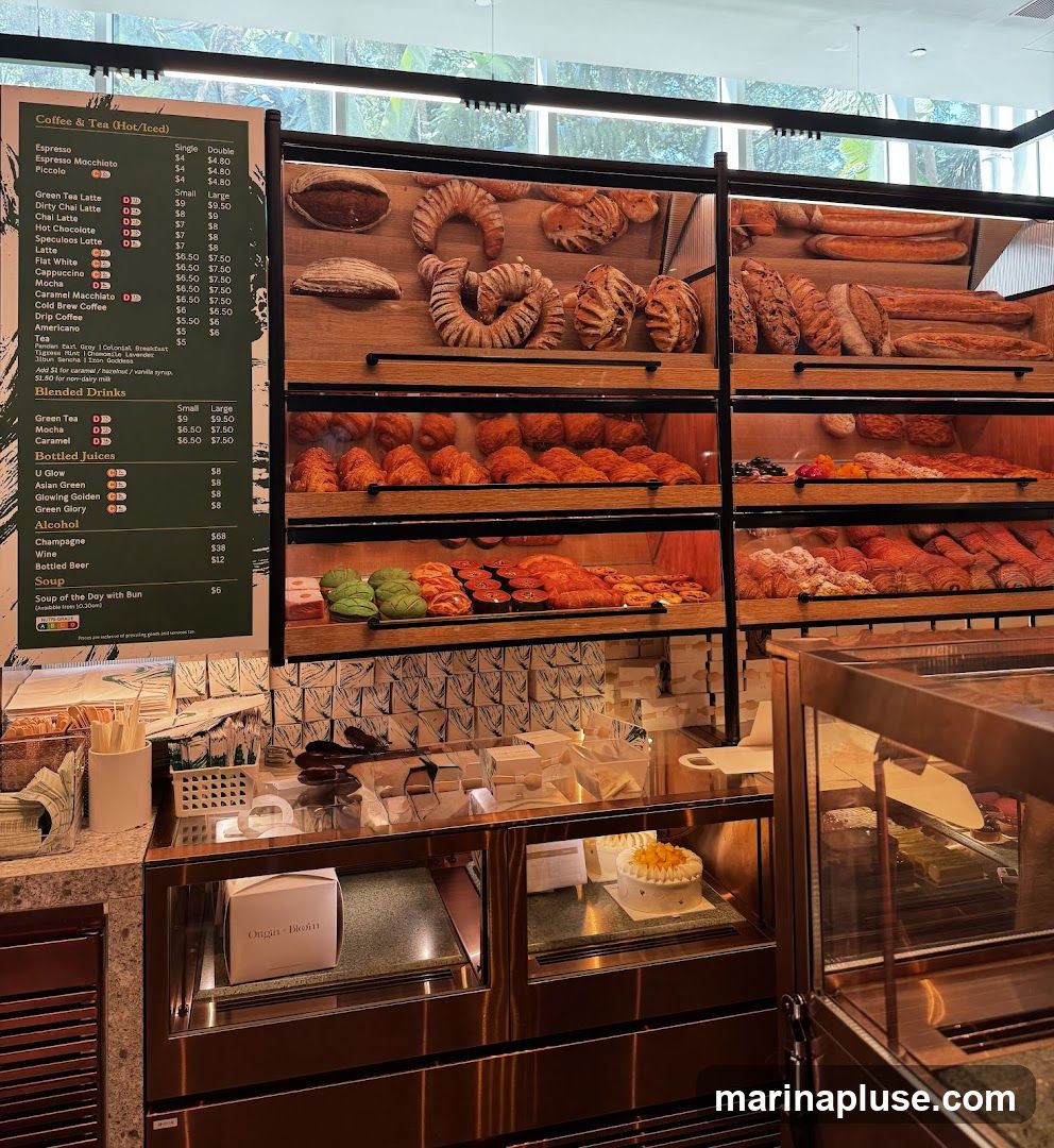 A display case filled with various baked goods, including loaves of bread, croissants, and pastries. A menu board is visible on the left side of the image, listing coffee, tea, blended drinks, juices, alcohol, and soup.