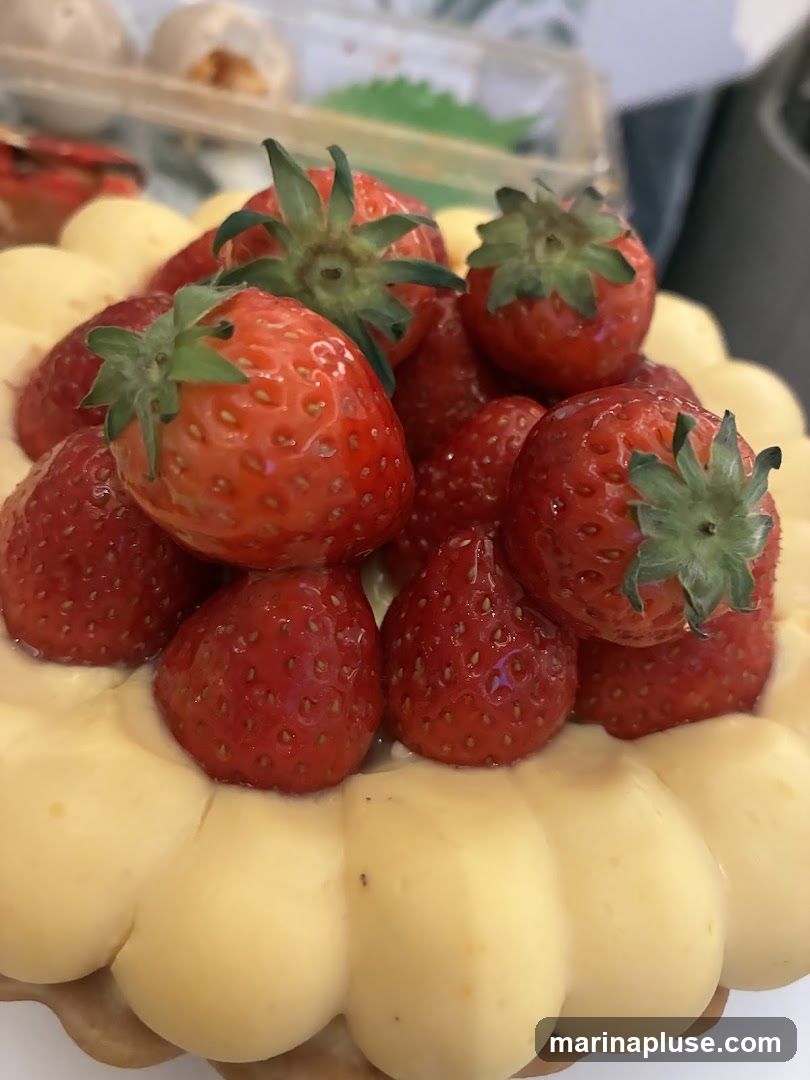 A close-up shot of a tart topped with fresh strawberries and a creamy yellow filling. The tart has a golden-brown crust and the strawberries are bright red and plump. The filling is piped in a decorative pattern around the edge of the tart.