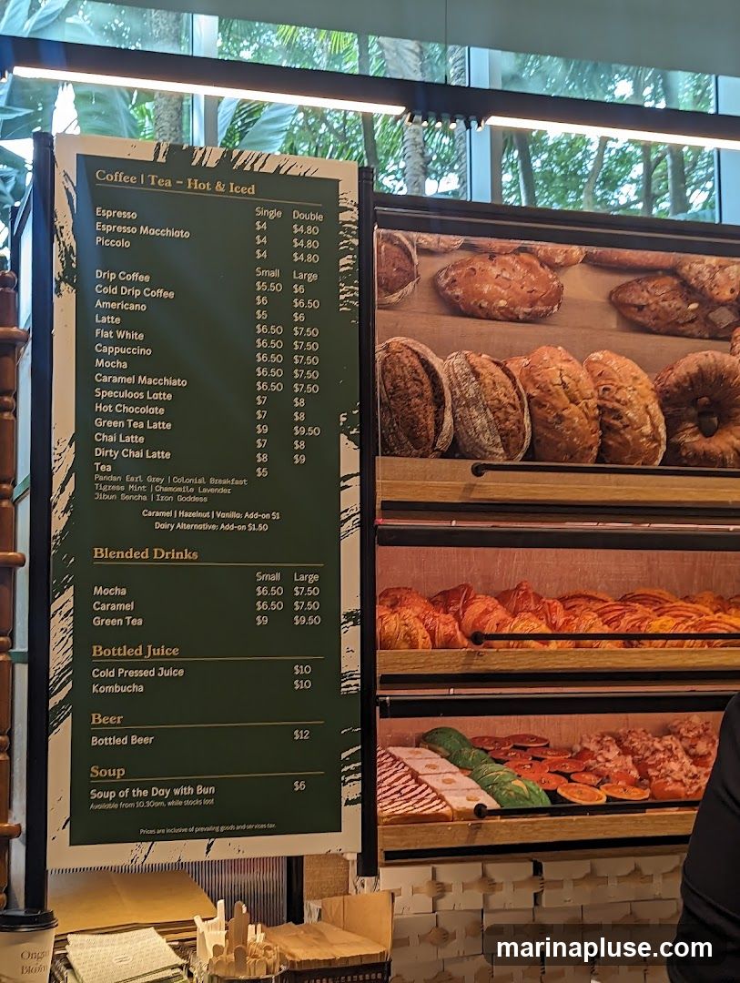 A menu board displays various coffee and tea options, including espresso drinks, drip coffee, and specialty lattes. It also lists blended drinks, bottled juices, bottled beer, and soup. The menu includes prices for single and double servings, as well as small and large sizes where applicable.
