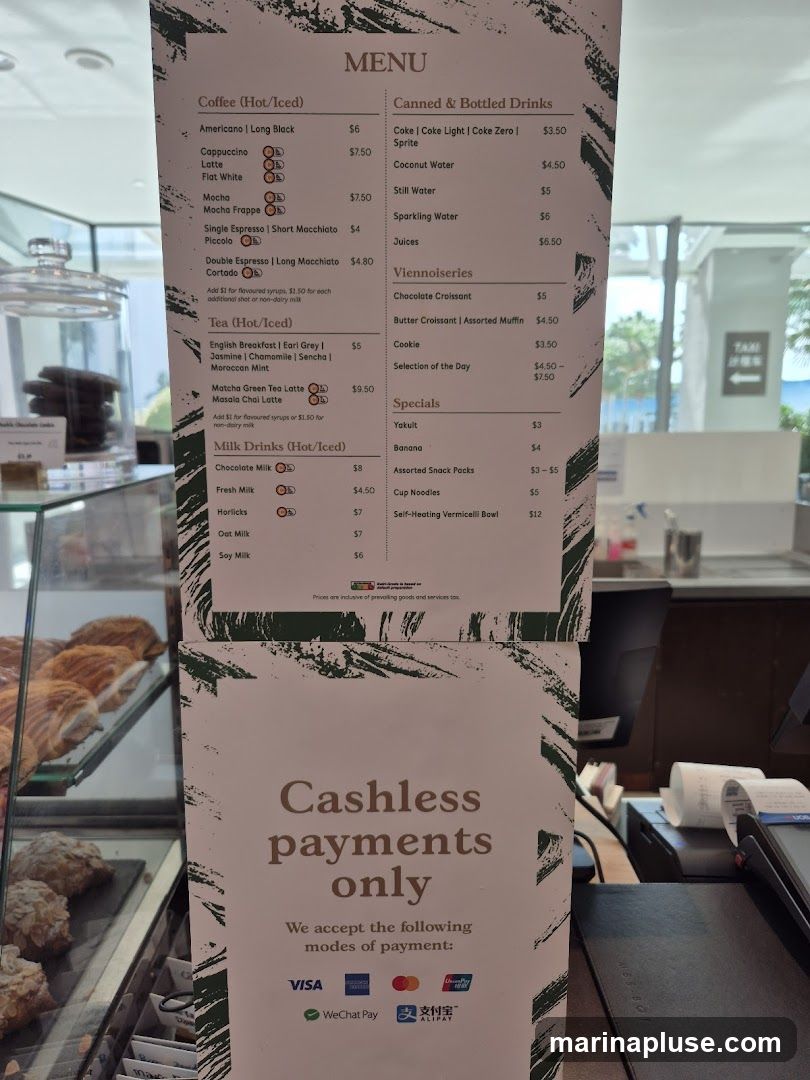 A menu board displaying coffee, tea, milk drinks, canned and bottled drinks, viennoiseries, and specials. It also indicates that cashless payments are accepted.