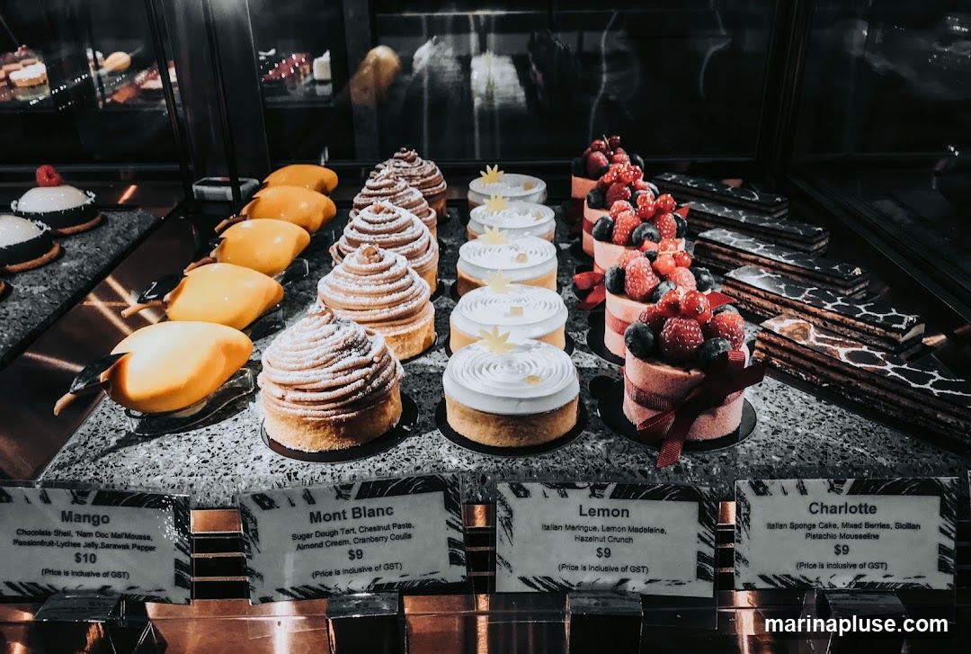 A display of various desserts in a refrigerated case, with individual labels and prices.