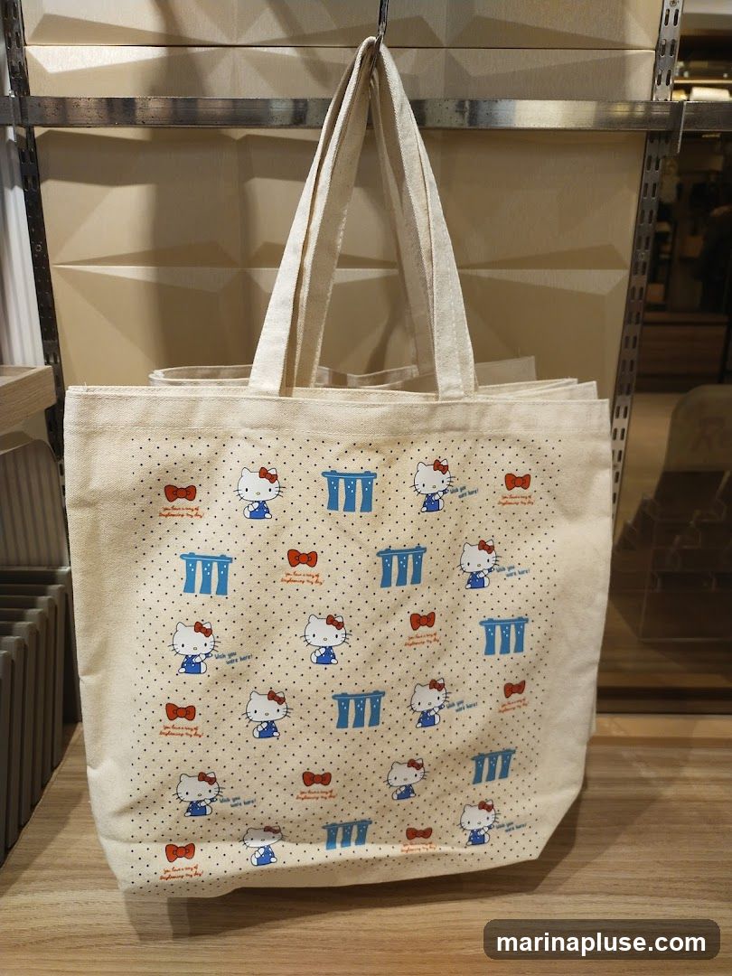 A cream-colored canvas tote bag with a repeating pattern of Hello Kitty characters, red bows, and blue structures. The bag is hanging from a metal rack.