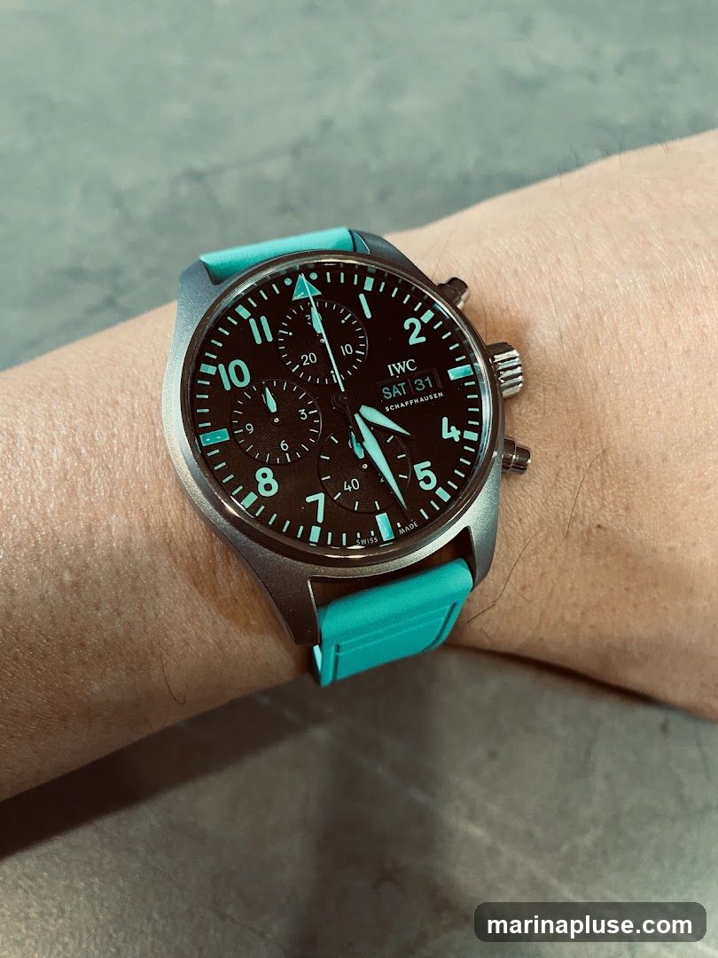 A close-up shot of a person's wrist wearing a dark-faced IWC Schaffhausen chronograph watch with a bright teal strap. The watch face has luminous Arabic numerals and hands, with sub-dials for chronograph functions. The date window shows "SAT 31". The watch is branded "IWC SCHAFFHAUSEN" and "MADE I SWISS".