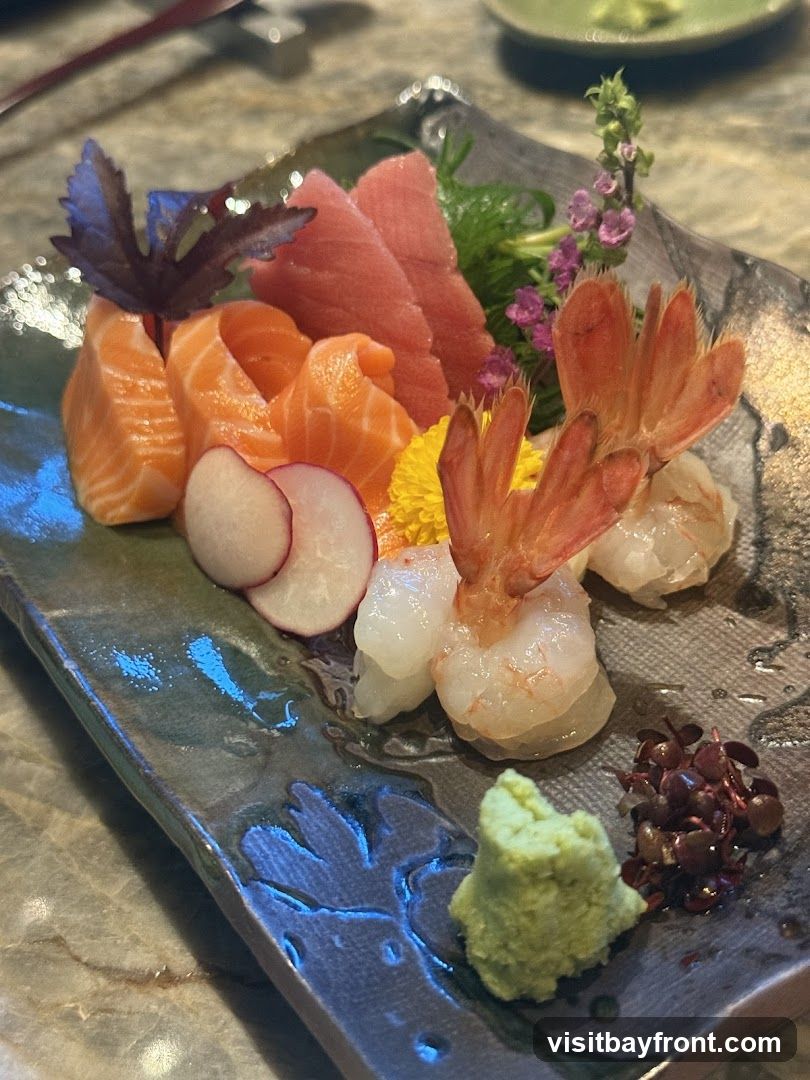 A close-up shot of a sashimi platter featuring slices of salmon and tuna, cooked shrimp, radish slices, wasabi, and garnishes.