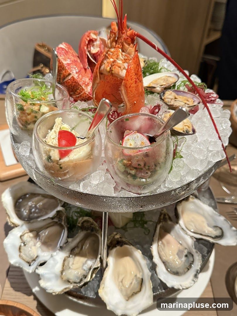 A tiered seafood platter featuring a whole lobster, oysters, clams, and various small dishes of seafood salad or ceviche, all served on a bed of crushed ice.