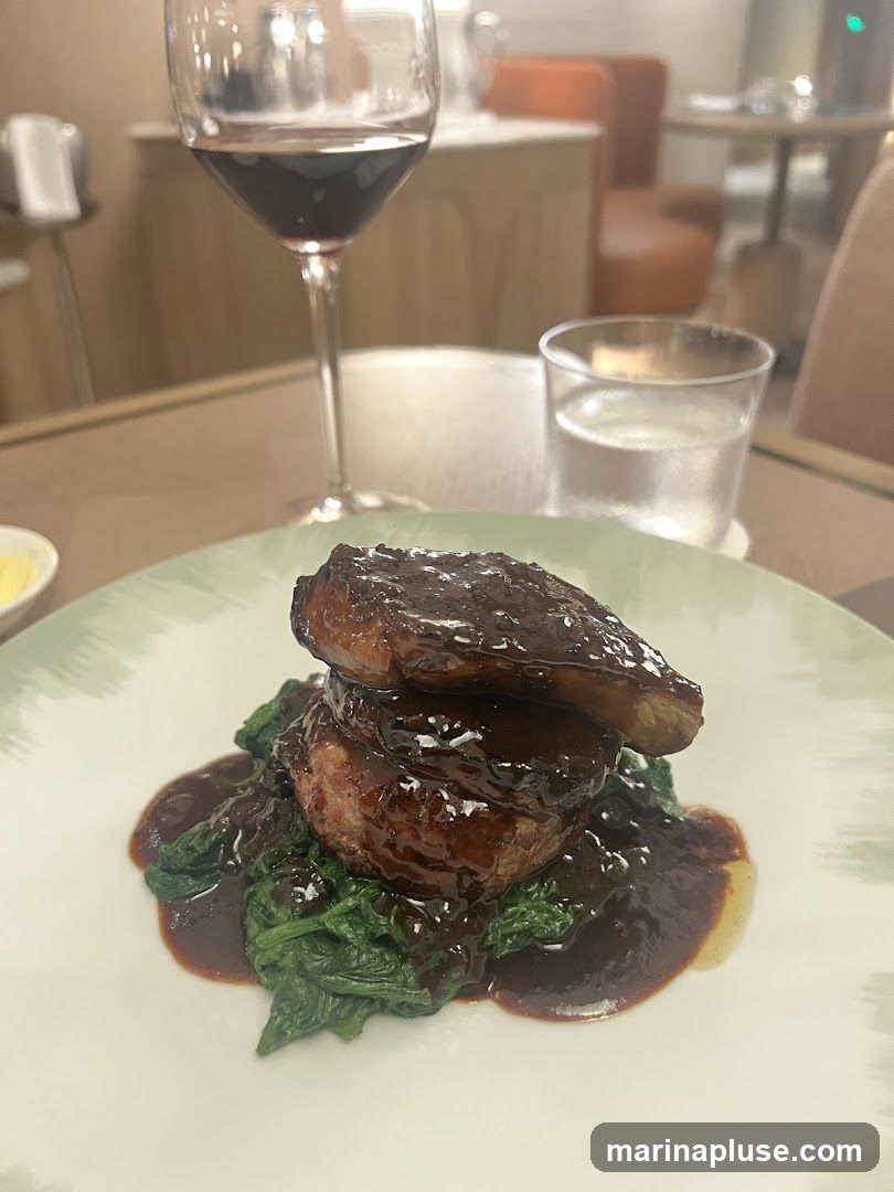 A plate of steak served with spinach and a dark sauce. A glass of red wine and a glass of water are on the table. The background shows a dining room setting with tables and chairs.