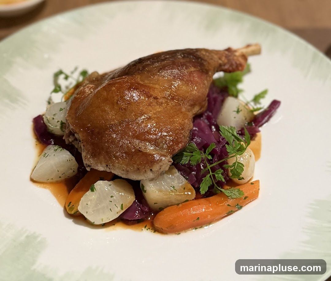A close-up shot of a plate of duck confit served with a medley of root vegetables, including red cabbage, carrots, and turnips. The duck leg is golden brown and crispy, resting on a bed of braised red cabbage and glazed root vegetables. Fresh parsley garnishes the dish. The plate has a subtle green, textured rim.