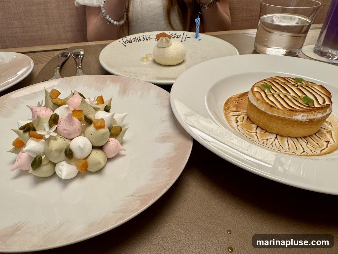 A close-up view of three desserts on a table. In the foreground, a white plate holds a colorful arrangement of meringue kisses in shades of white, pink, and green, interspersed with chopped pistachios and dried fruit. To the right, another white plate features a tart with a golden crust and a topping of toasted meringue, garnished with mint leaves. In the background, a round white plate has a small white dessert with a dollop of orange topping and a blue birthday candle. A glass of water and a purple drink are also visible.
