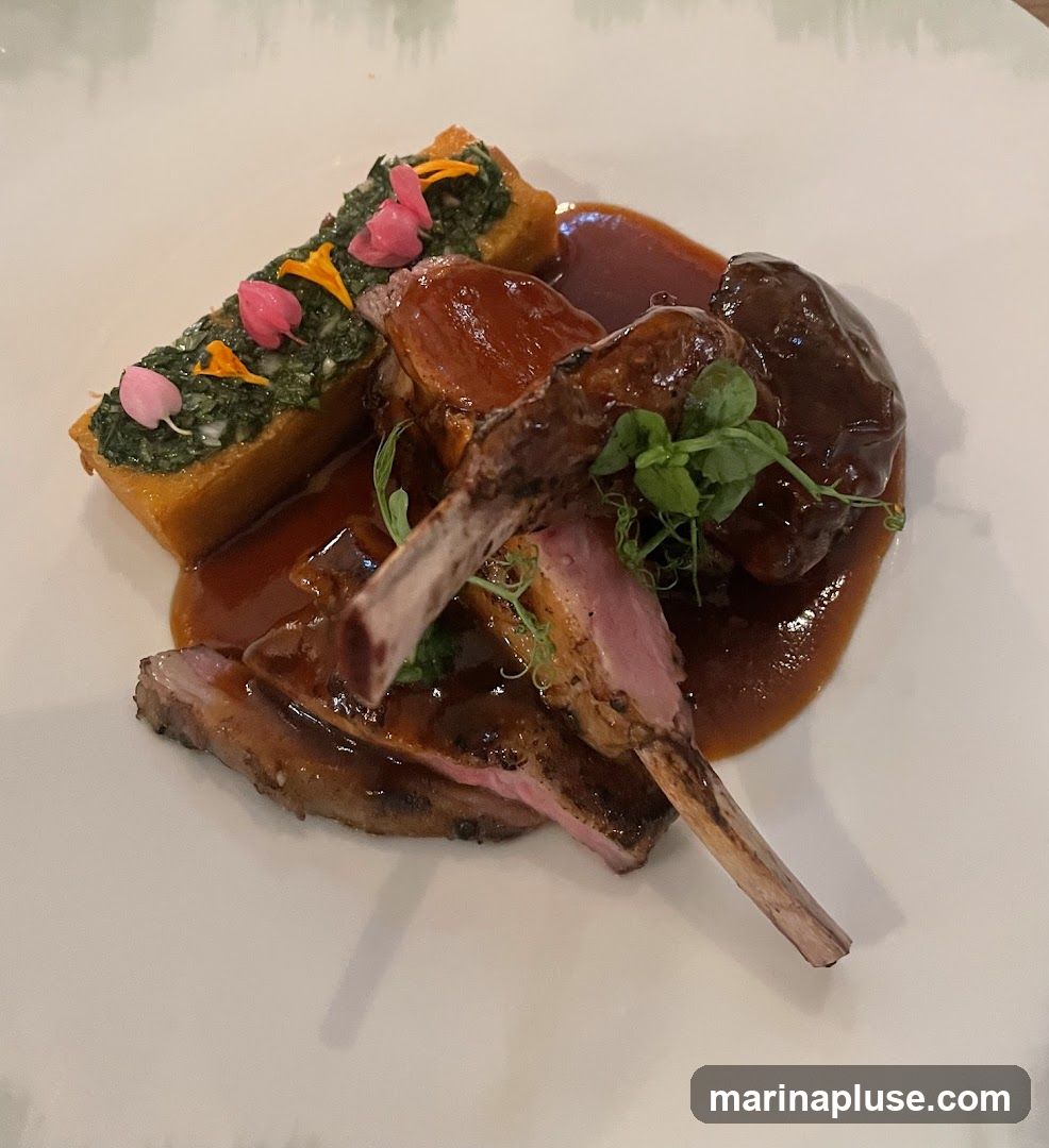 A plate of lamb chops served with a rectangular piece of polenta topped with chopped greens and edible flowers, all coated in a rich brown sauce.
