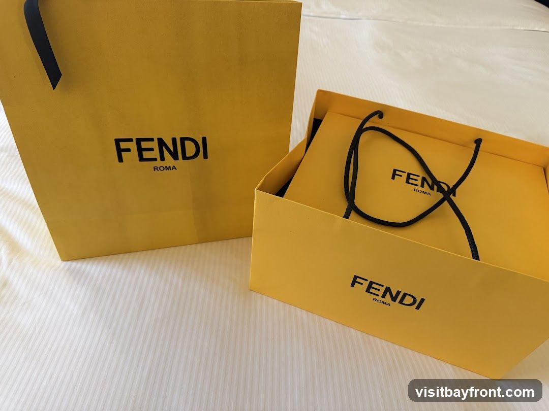 Two yellow Fendi shopping bags, one open and one closed, are placed on a white, textured surface. Both bags feature the Fendi Roma logo in black lettering.
