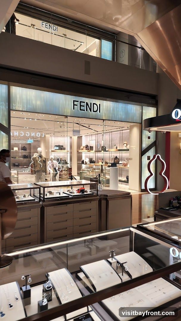 The exterior of a Fendi store with the Fendi logo prominently displayed above the entrance. Inside, handbags and accessories are showcased on shelves and display cases. In the foreground, glass display cases exhibit jewelry.