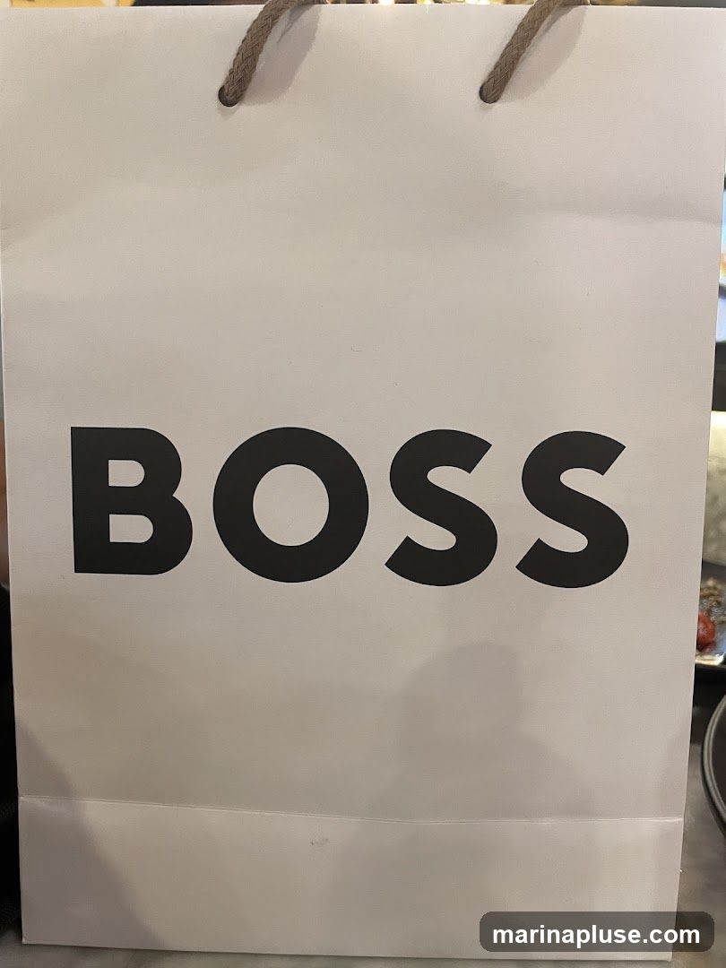 A white shopping bag with the word "BOSS" printed in large black letters. The bag has braided rope handles.