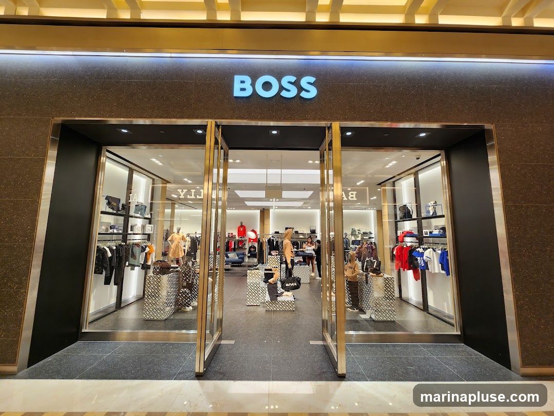 The exterior of a BOSS store with large glass doors and windows. The store name "BOSS" is displayed in large blue letters above the entrance. Inside, clothing and accessories are displayed on shelves and racks.