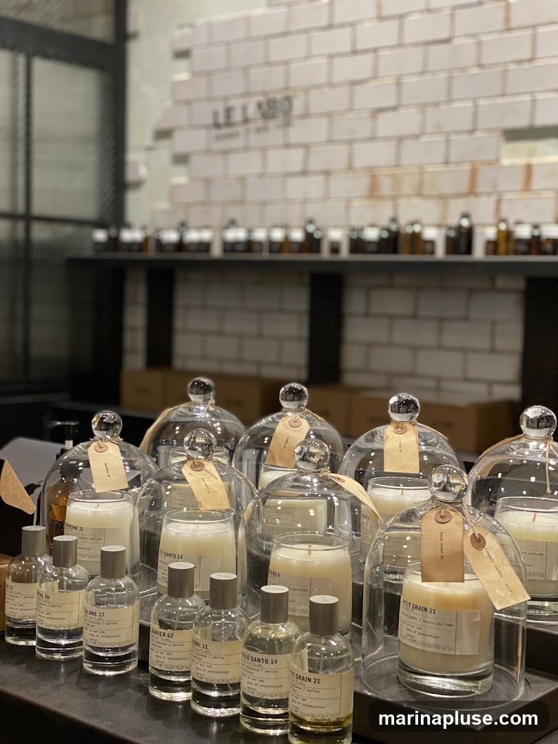 A display of candles under glass domes and various perfume bottles on a dark surface. The background features a white brick wall with the text "LELAB" visible.