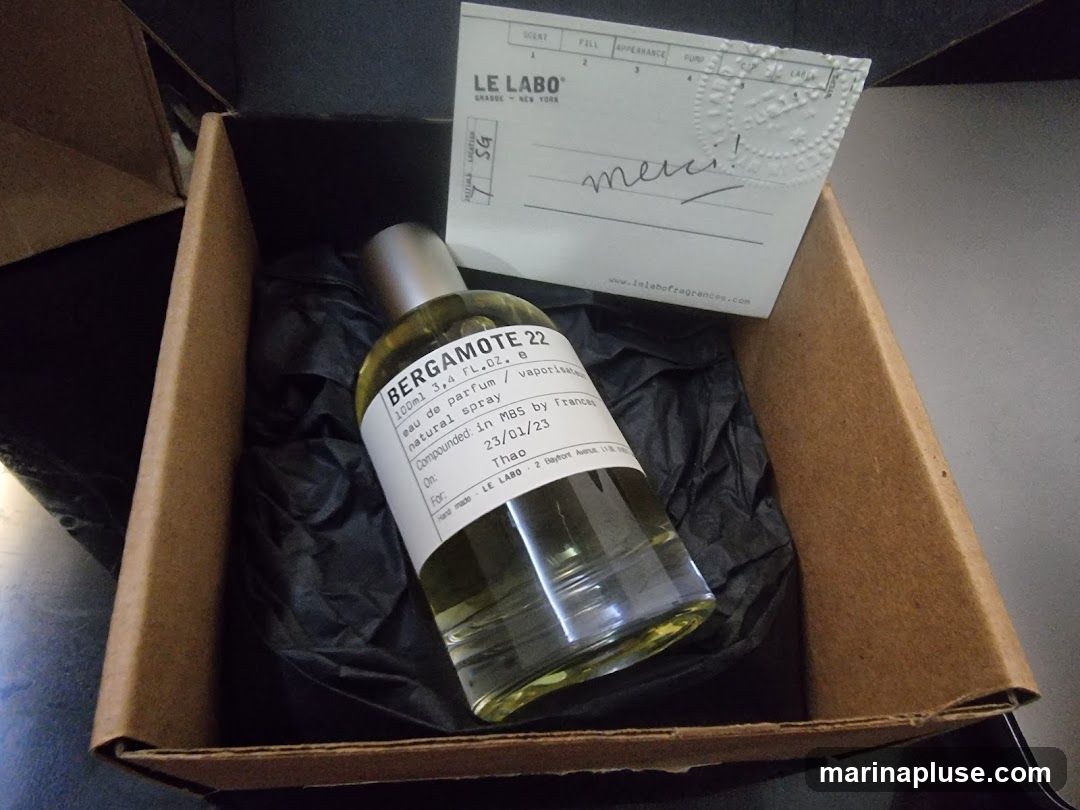 A bottle of Le Labo Bergamote 22 perfume is presented in a cardboard box lined with black tissue paper. A small card with the Le Labo logo and a handwritten "merci!" is placed on top of the perfume bottle. The bottle label indicates it is a 100ml natural spray eau de parfum, compounded on 23/01/23 for Thao.