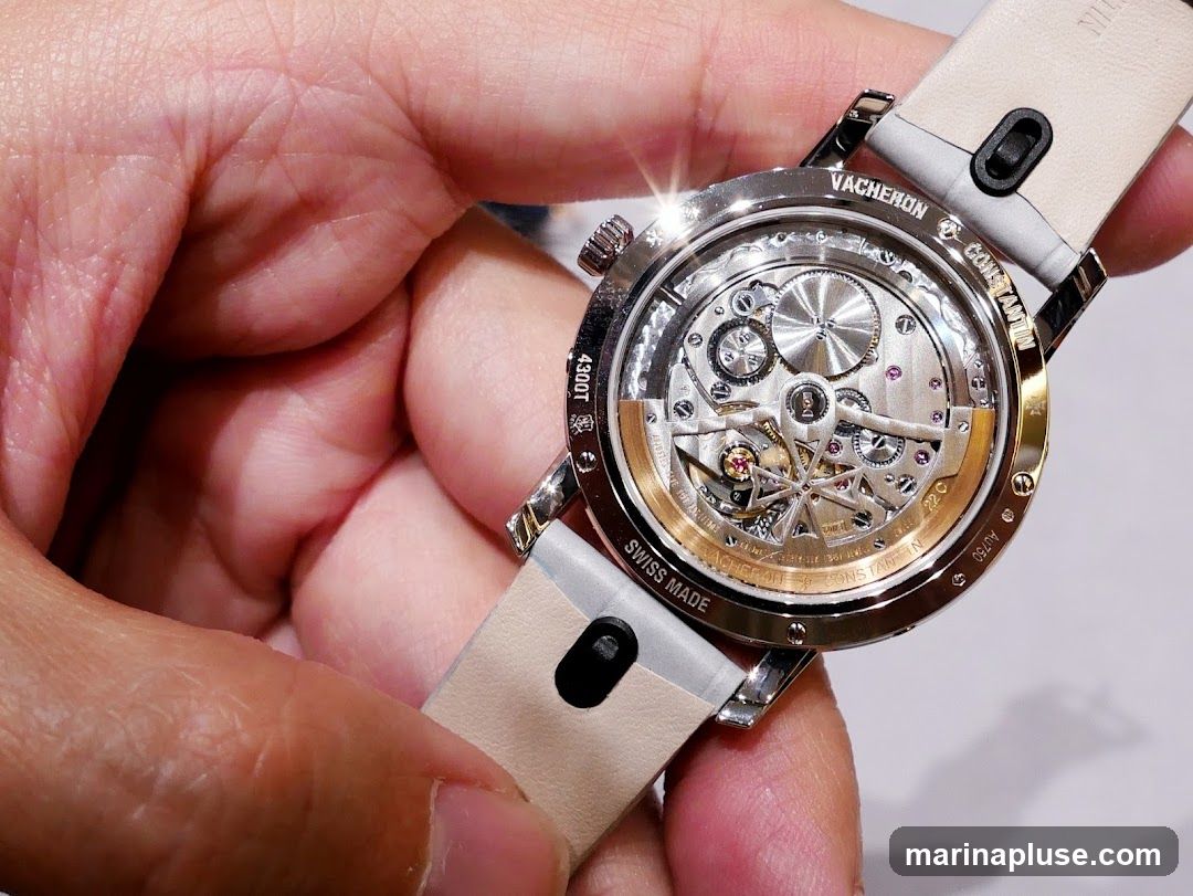 A close-up shot of the intricate mechanical movement of a Vacheron Constantin watch, held by a person's hand. The watch case is open, revealing the gears, springs, and jewels of the timepiece. The brand name "VACHERON CONSTANTIN" is visible on the watch case, along with "SWISS MADE" and "AU750".