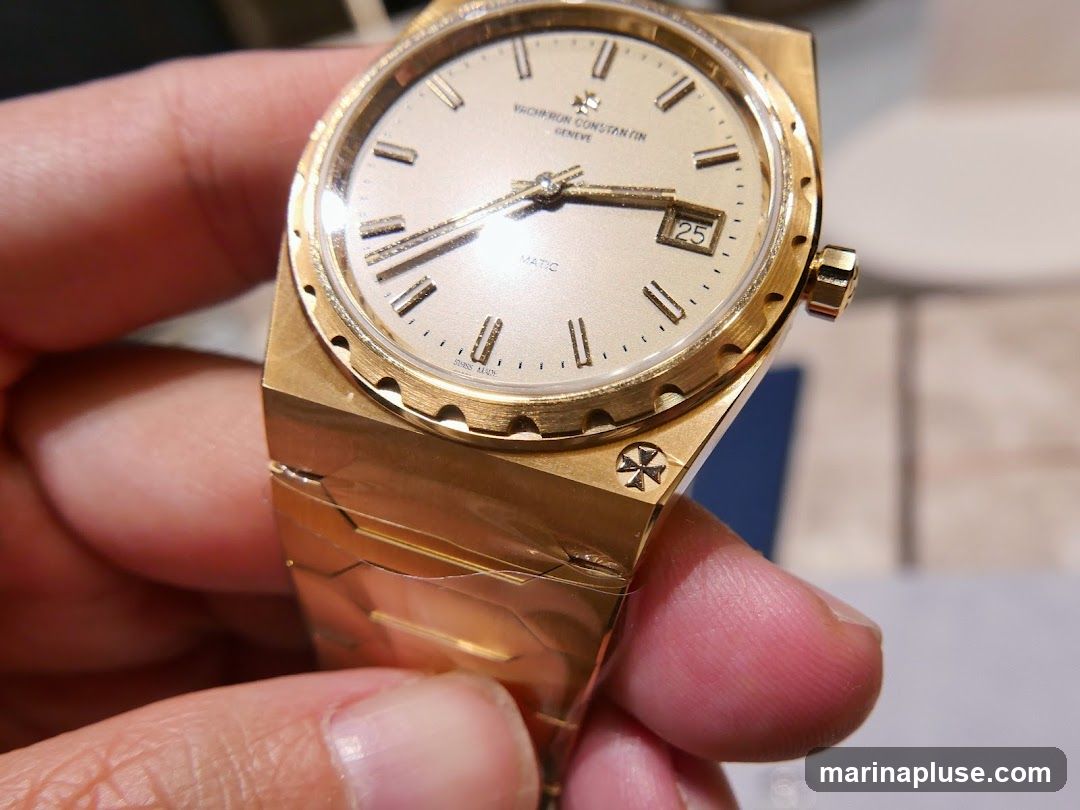 A close-up shot of a gold Vacheron Constantin watch being held by a person. The watch face is light-colored with gold hands and hour markers. Roman numerals are visible for some hours. The date window shows '25'. The watch band is also gold and has a distinctive segmented design. The Vacheron Constantin logo, a Maltese cross, is visible on the watch case.