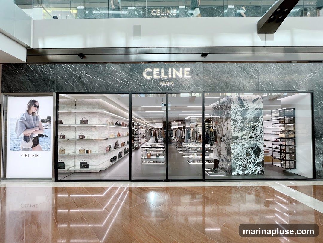 The exterior of a Celine store with a large glass facade. The store displays handbags and clothing on shelves. A large advertisement featuring a model wearing a Celine scarf is on the left side of the entrance. The Celine Paris logo is visible above the entrance.