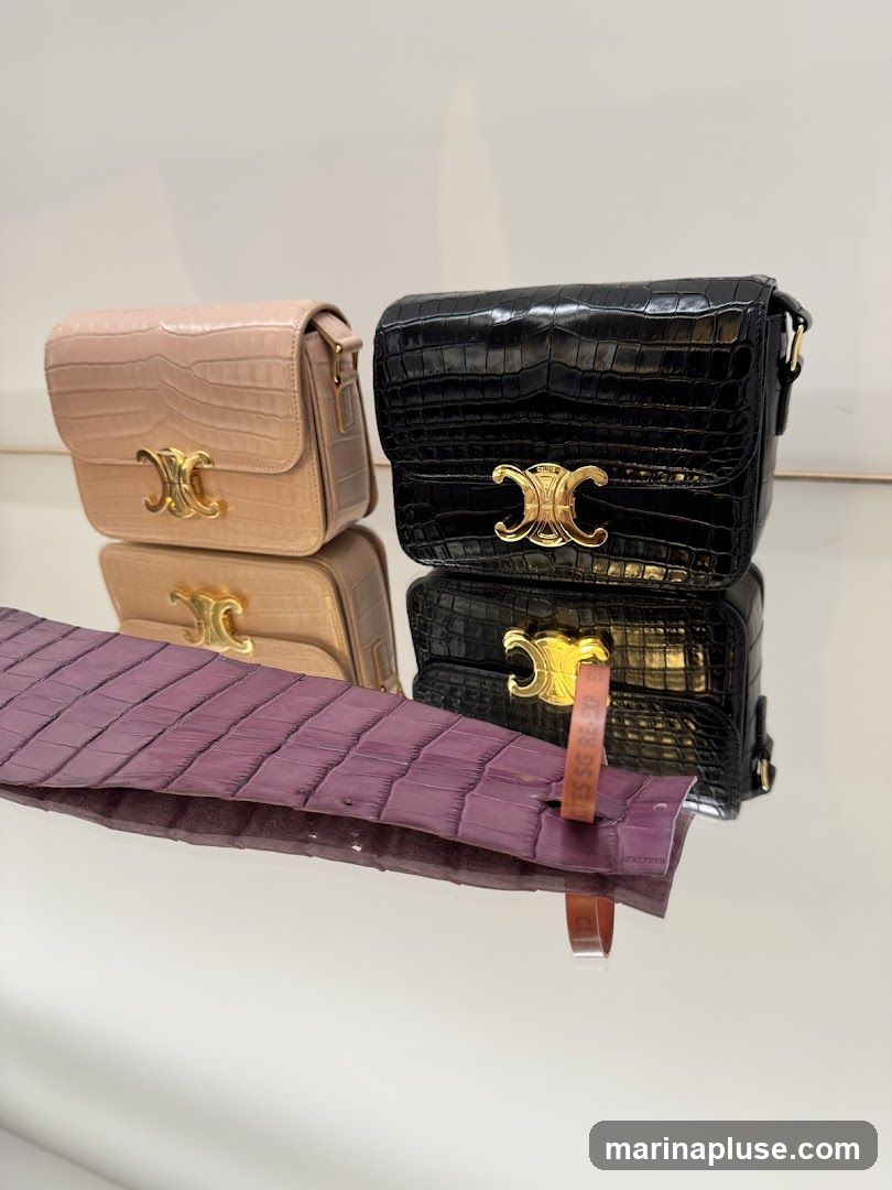 Two crocodile-embossed leather handbags, one in a light pinkish-beige and the other in black, are displayed on a reflective surface. Both bags feature a gold-toned Triomphe logo closure. In the foreground, a strip of purple crocodile leather is visible, with a small orange tag attached.