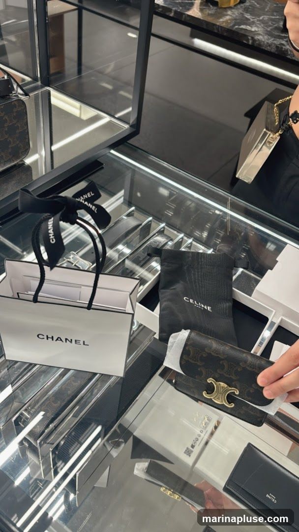 A display case in a luxury retail store showcasing Chanel shopping bags and Celine branded items, including a wallet and a small pouch.