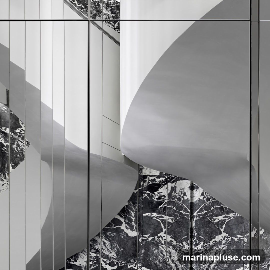 An abstract close-up of a modern architectural interior featuring a juxtaposition of smooth, curved white surfaces and dark, veined marble. The composition is dominated by reflections in mirrored panels, creating a sense of depth and visual complexity. The interplay of light and shadow highlights the organic forms and the rich texture of the marble.