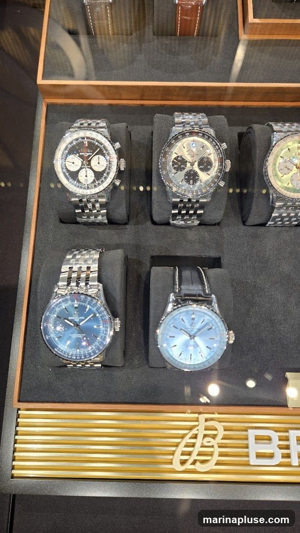 A display case featuring several Breitling watches. The watches have metal bands and various dial colors, including black, silver, and blue. The display includes the Breitling logo at the bottom.