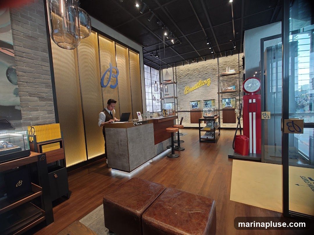 The interior of a Breitling store, featuring a reception desk with a staff member, display cases with watches, and decorative elements like a vintage gas pump. The store has a modern and luxurious ambiance with wooden floors and brick walls.
