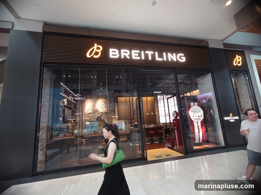 A Breitling watch store with large glass windows displaying watches and store interiors. The store's name and logo are prominently displayed on the facade. People are walking by the storefront.