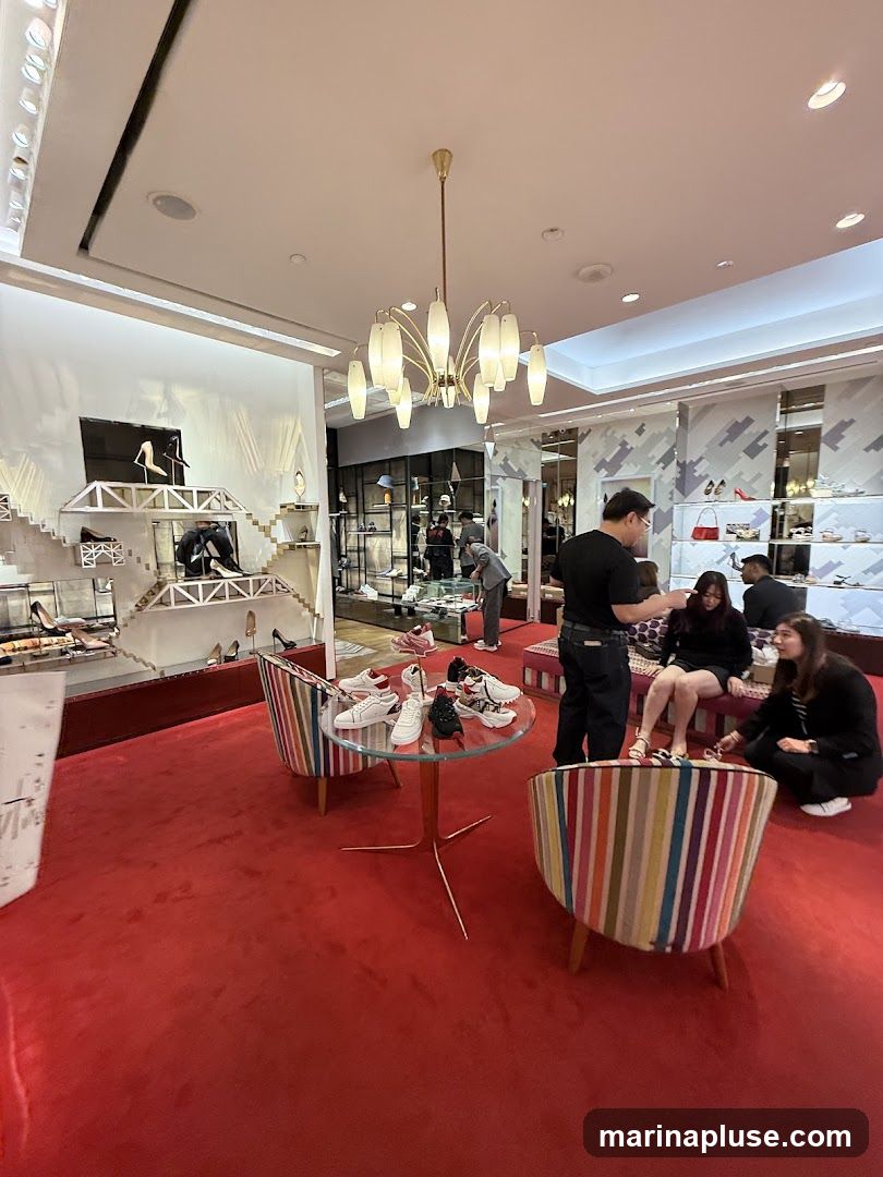 A brightly lit shoe store with a red carpet and display shelves filled with various shoes. Several customers are browsing, and a salesperson is assisting a group. A glass table in the foreground displays a selection of sneakers.