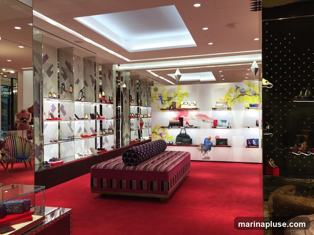 The interior of a high-end shoe store with red carpeting and brightly lit display shelves showcasing various women's shoes and handbags. A decorative sofa with a patterned cushion is placed in the foreground. The walls feature artistic murals of birds and foliage. Mirrors are used extensively to enhance the sense of space.
