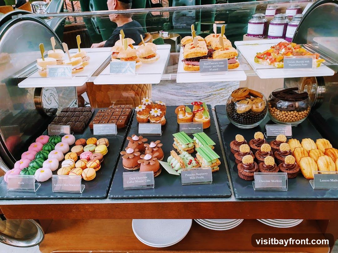A display of various desserts and small bites, including mini sandwiches, macarons, cakes, and pastries, arranged on tiered shelves.