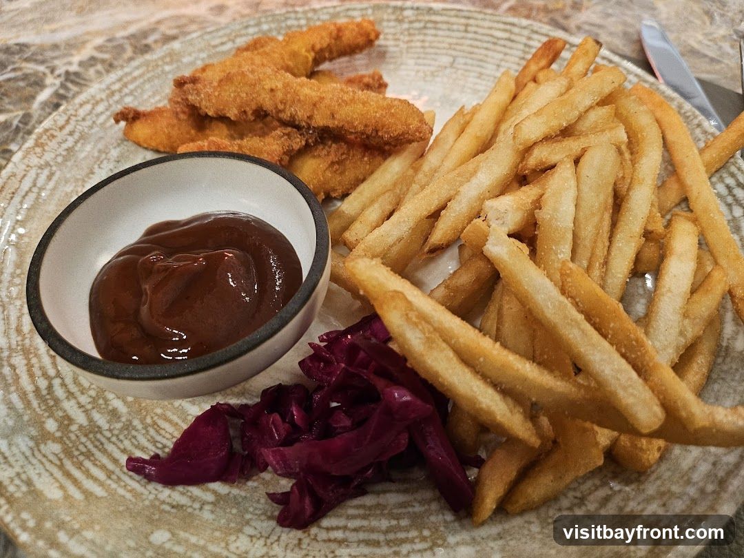 A plate of crispy chicken tenders, french fries, a small bowl of barbecue sauce, and a side of shredded red cabbage.