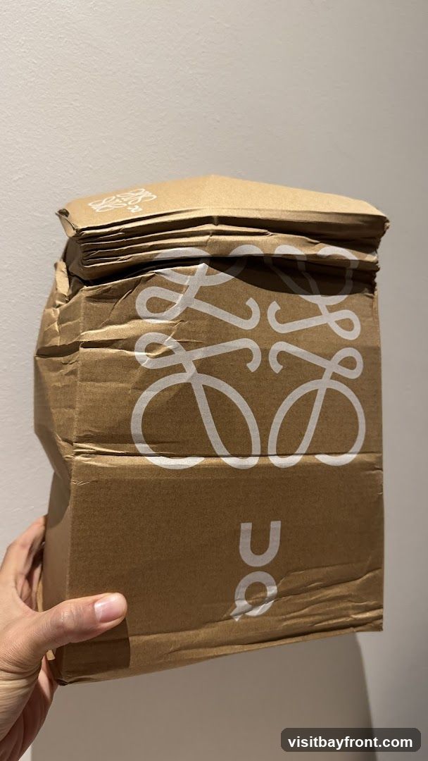 A hand holds a crumpled brown paper bag with the Loewe logo printed in white. The bag appears to be a shopping bag or packaging from the luxury fashion brand.