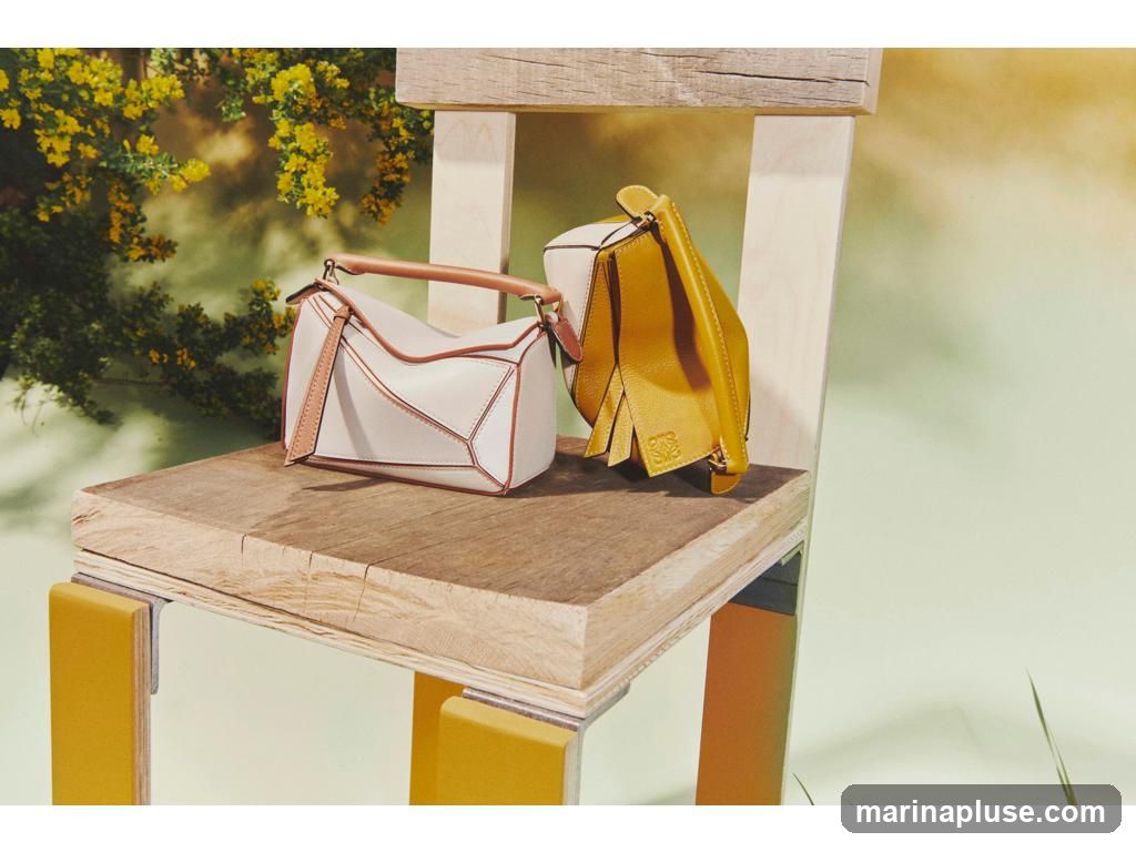 Two designer handbags, one cream and tan, the other yellow, are displayed on a rustic wooden chair. The cream bag has a geometric design and tan leather trim and handles. The yellow bag is folded and has a fringe detail. A small embossed logo is visible on the yellow bag. The background features blurred yellow flowers and greenery, with a soft, gradient light.