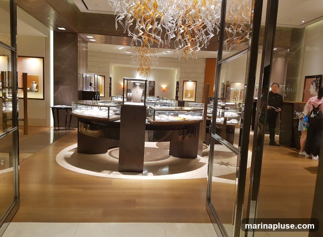 The interior of a well-lit jewelry store with display cases filled with jewelry. A large, ornate chandelier hangs from the ceiling. Several customers and staff members are visible.
